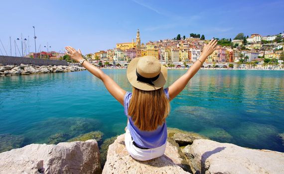 Traveling in France. Panoramic view of traveler girl with arms raised enjoying view of Menton village, French Riviera.