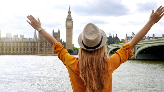 Enthusiastic traveler student girl with raised arms in London enjoying the view of mains attractions, UK