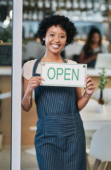 Opening shop for the day. Portrait of a young woman holding an open sign in a cafe.