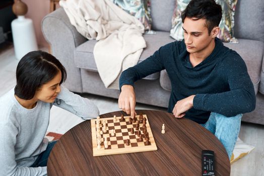How is your lockdown going to play out. a young couple playing a game of chess at home.