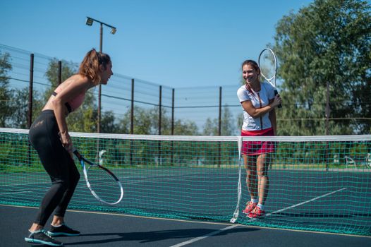 Two athletic young women play tennis on an outdoor court on a hot summer day.