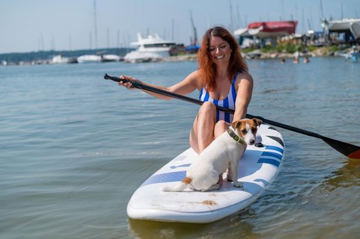 Young red-haired woman on a paddle board with her dog. Surfing