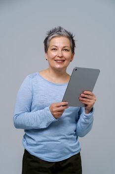 Mature grey haired woman holding digital tablet working or shopping online, checking on social media. Pretty woman in blue blouse isolated on white background