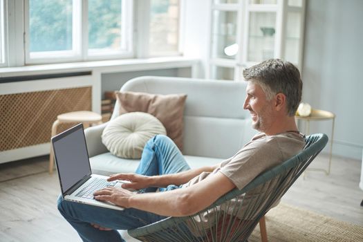 cropped image of a man using a laptop while sitting in a chair.