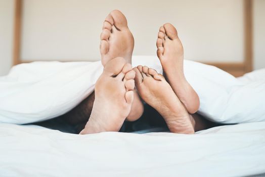 Feet of an in love couple lying in bed, relaxing and bonding together at home. Closeup of a barefoot boyfriend and girlfriend sleeping, resting or taking a nap in their bedroom