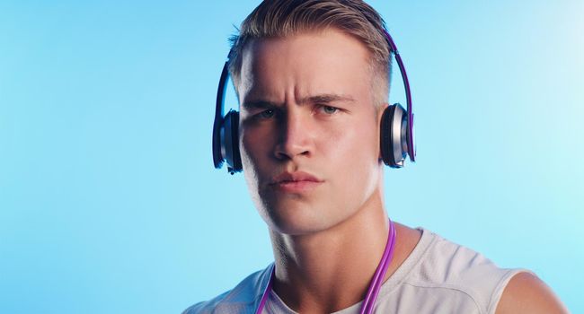 Im ready for a workout. Studio portrait of a young man posing with a skipping rope and headphones against a blue background.