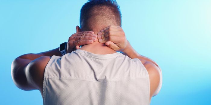 Injury is a risk of exercise. Rearview shot of an unrecognizable young man rubbing his neck in pain against a blue background.