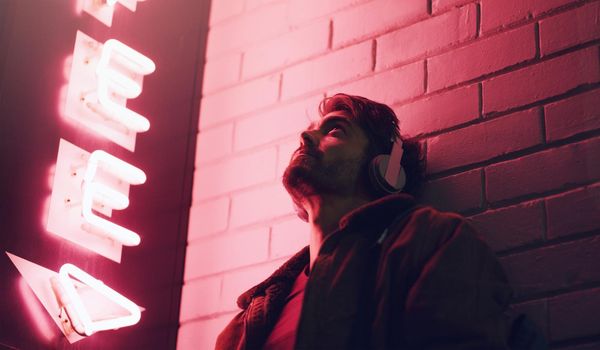 Put on your headphones and forget everything else. a young man wearing headphones while leaning against a building at nighttime.