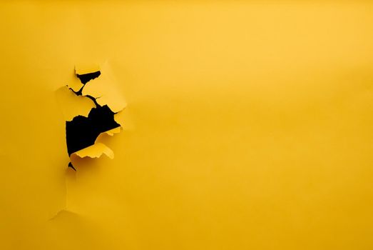Hole with torn edges in yellow paper, full frame. 