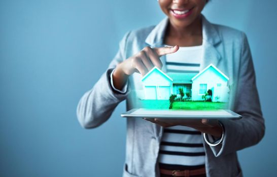 Corporate business woman holding a tablet with property cgi graphics while standing against a blue studio background alone. Happy, smiling and cheerful female designing a vr home with technology