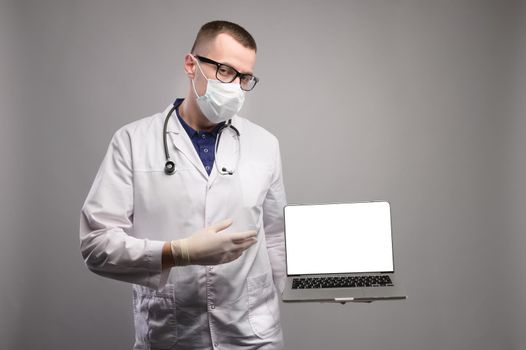 Young male doc in white coat pointing at blank laptop screen, studio shot