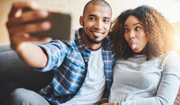 Funny and silly couple taking selfie and making goofy face at phone for social media post while relaxing. Boyfriend and girlfriend having fun and enjoying time together at home and sharing it online