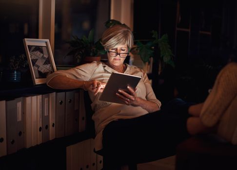 Deadlines met. Time to put your feet up. an attractive mature businesswoman looking relaxed while using her tablet late at night in the office.
