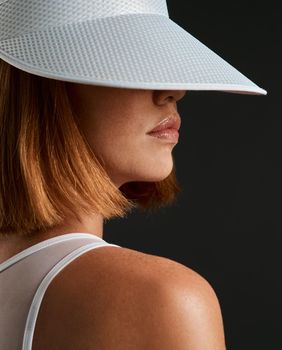 Ill see you out on the court. a sporty young woman wearing a sun visor against a dark background.