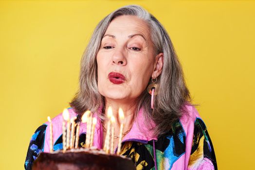 Dont count the years, make the years count. a confident and stylish senior woman holding her birthday cake against a yellow background.