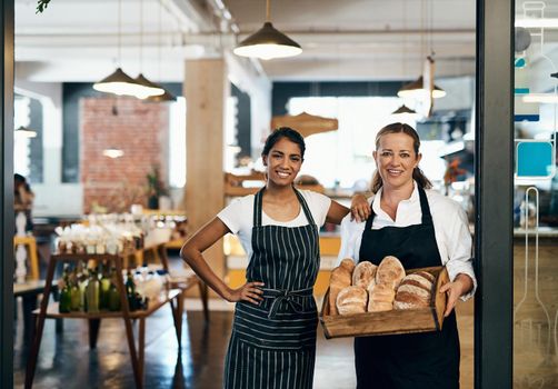 Nobody gets bread like we do. two women holding a selection of freshly baked breads in their bakery.
