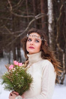 Beautiful bride in a white dress with a bouquet in a snow-covered winter forest. Portrait of the bride in nature.