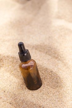 Cosmetic serum in a glass bottle with a pipette in the sand