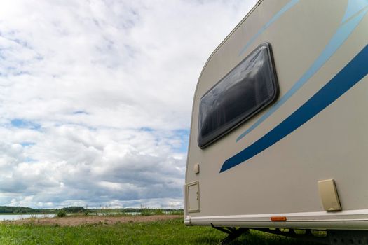 Camper trailer for traveling standing on shore of the lake in summer