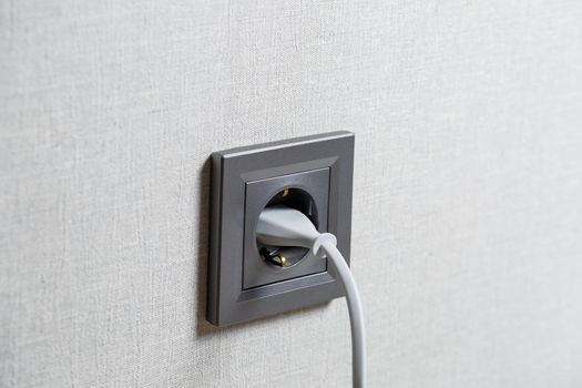 A gray outlet on the wall which includes a device with a white cord. Charging from a power outlet