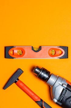 Tools for repairing home use. Hammer for nails, level and drill on an orange background. Toolkit for the wizard