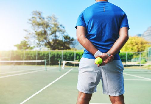 Got game Lets play. Rearview shot of an unrecognizable male tennis player holding a tennis ball on a court outdoors.