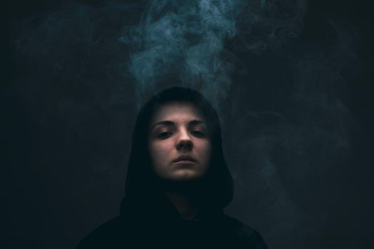 Dark portrait of a short haired girl wearing hoodie with smoke coming out of it. .