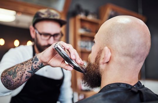 A little trim wont hurt. a handsome young barber trimming and lining up a clients beard inside his barbershop.