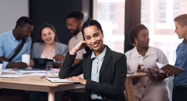 Skill and confidence are an unconquered army. Portrait of a young businesswoman sitting in an office with her colleagues in the background.