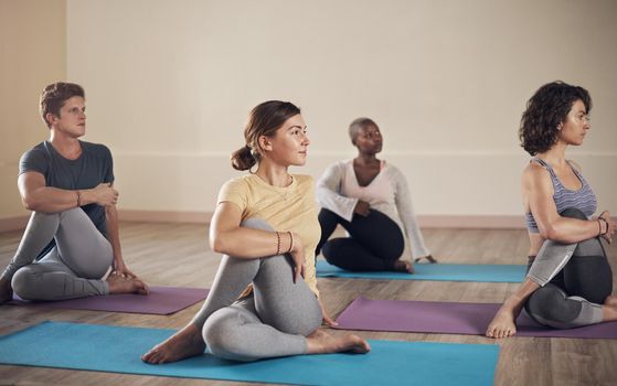 Releasing the tension from my spine. Full length shot of a diverse group of yogis holding a spinal half twist pose during an indoor yoga session.