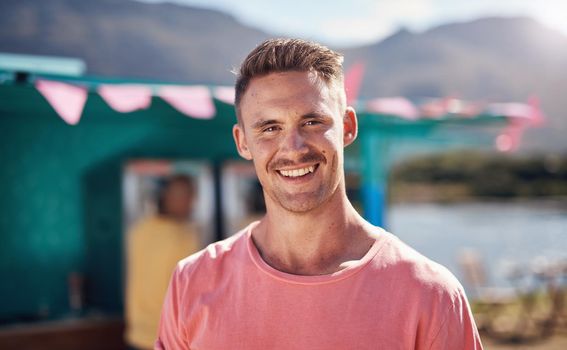 Nothing like the open air. Portrait of a cheerful young man smiling brightly while standing outside on a beach promenade during the day.