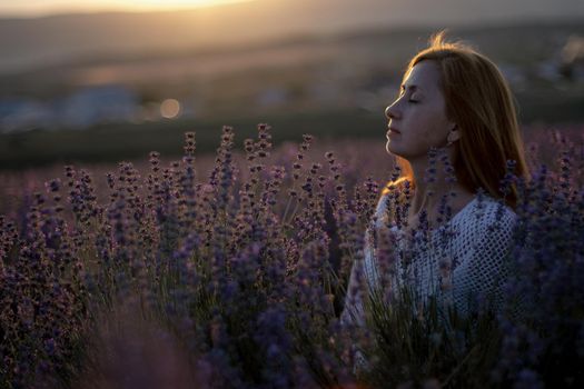 A middle-aged woman sits in a lavender field and enjoys aromatherapy. Aromatherapy concept, lavender oil, photo session in lavender
