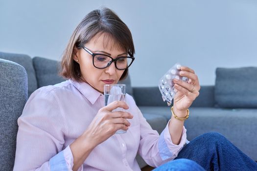 Mature sick woman taking pills with a glass of water