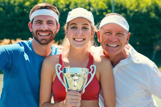 Post victory picture is necessary. Cropped portrait of a group of sportspeople standing together and holding a trophy after winning a tennis match.
