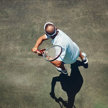 A perfect back swing. High angle shot of a focused middle aged man playing tennis outside on a tennis court during the day.