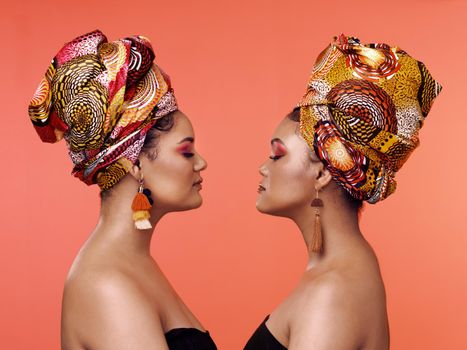 African Queens. Studio shot of two attractive young women wearing traditional African head wraps posing together against an orange background.