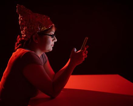 Paranoid caucasian woman using smartphone wearing tinfoil hat. Conspiracy theory.