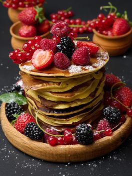 A stack of pancakes with fresh fruits poured with syrup on a black background