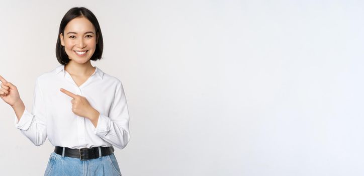 Image of smiling young office lady, asian business entrepreneur pointing fingers left, showing client info, chart of banner aside on copy space, white background