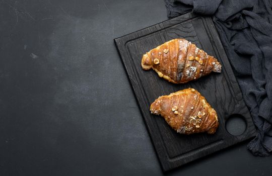 Baked croissant on a  board and sprinkled with powdered sugar, black table. Appetizing pastries for breakfast	