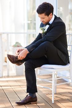 Time to step into a new chapter in my life. Full length shot of a handsome young bridegroom sitting on a chair and tying his shoelaces on his wedding day.