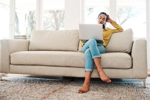 Trying to decide which blog will attract more followers. Full length shot of an attractive young businesswoman sitting on her couch and blogging from her laptop while at home.