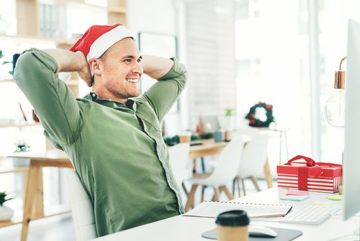 Im watching everything fall into place. a young businessman relaxing with his hands behind his head while working in his office on Christmas Eve.