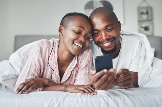 Something aww to start the day. a happy young couple using a smartphone together in the bedroom at home.