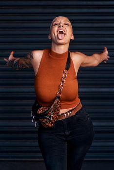 Shes all the fun she could ever need. an attractive young woman sticking out her tongue while standing with her arms outstretched against a dark background.