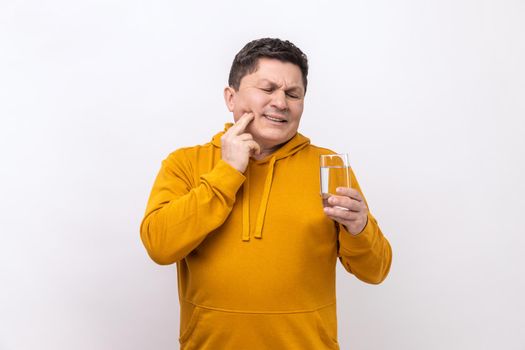 Portrait of unhealthy middle aged man having teeth pain after drinking water from glass, dental injury, wearing urban style hoodie. Indoor studio shot isolated on white background.