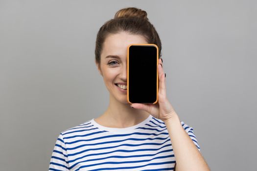 Woman covering eye with cell phone with empty display for advertisement.