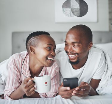 Its the small moments that mean a lot. a happy young couple using a smartphone and having coffee together in the bedroom at home.