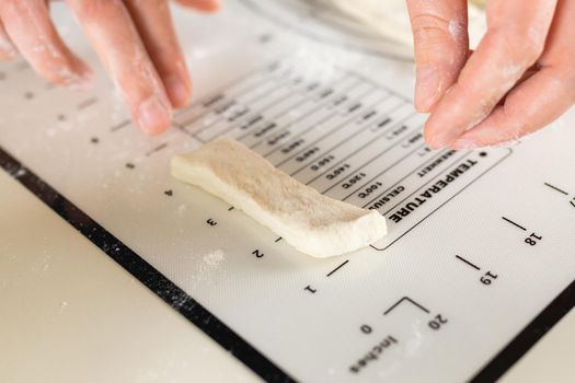Cook's hands measuring the length in inches of a cut piece of dough on a kitchen mat with markings, selective focus and close-up
