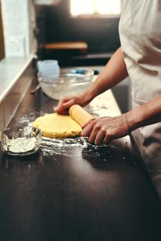 This will be definitely baked to perfection. an unrecognizable woman flattening dough with a rolling pin while baking inside her kitchen at home.